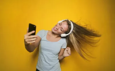 Eine Frau tanzt mit einem Smartphone vor einem gelben Hintergrund